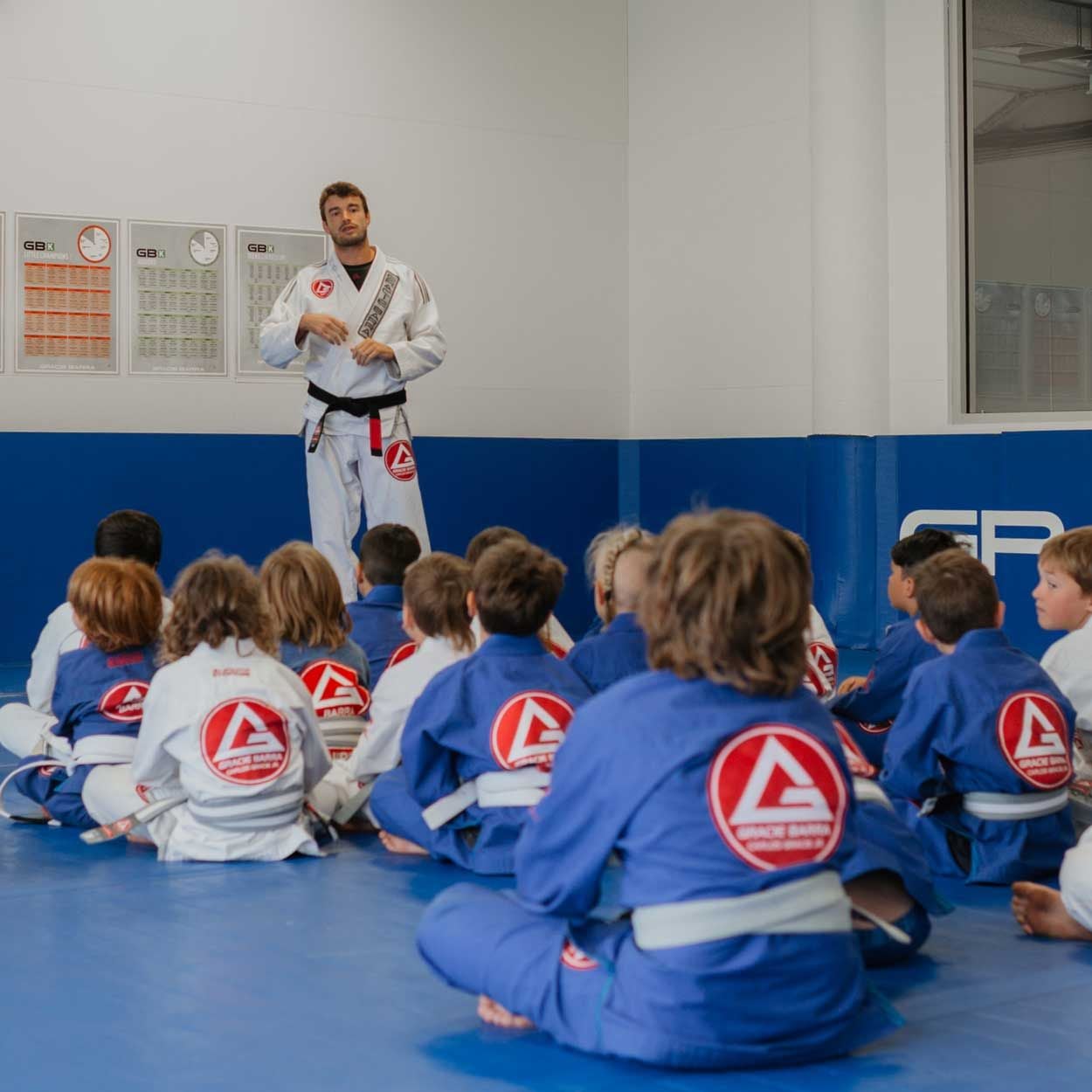 Young students sitting cross-legged, listening to their Gracie Barra Burleigh Heads instructor